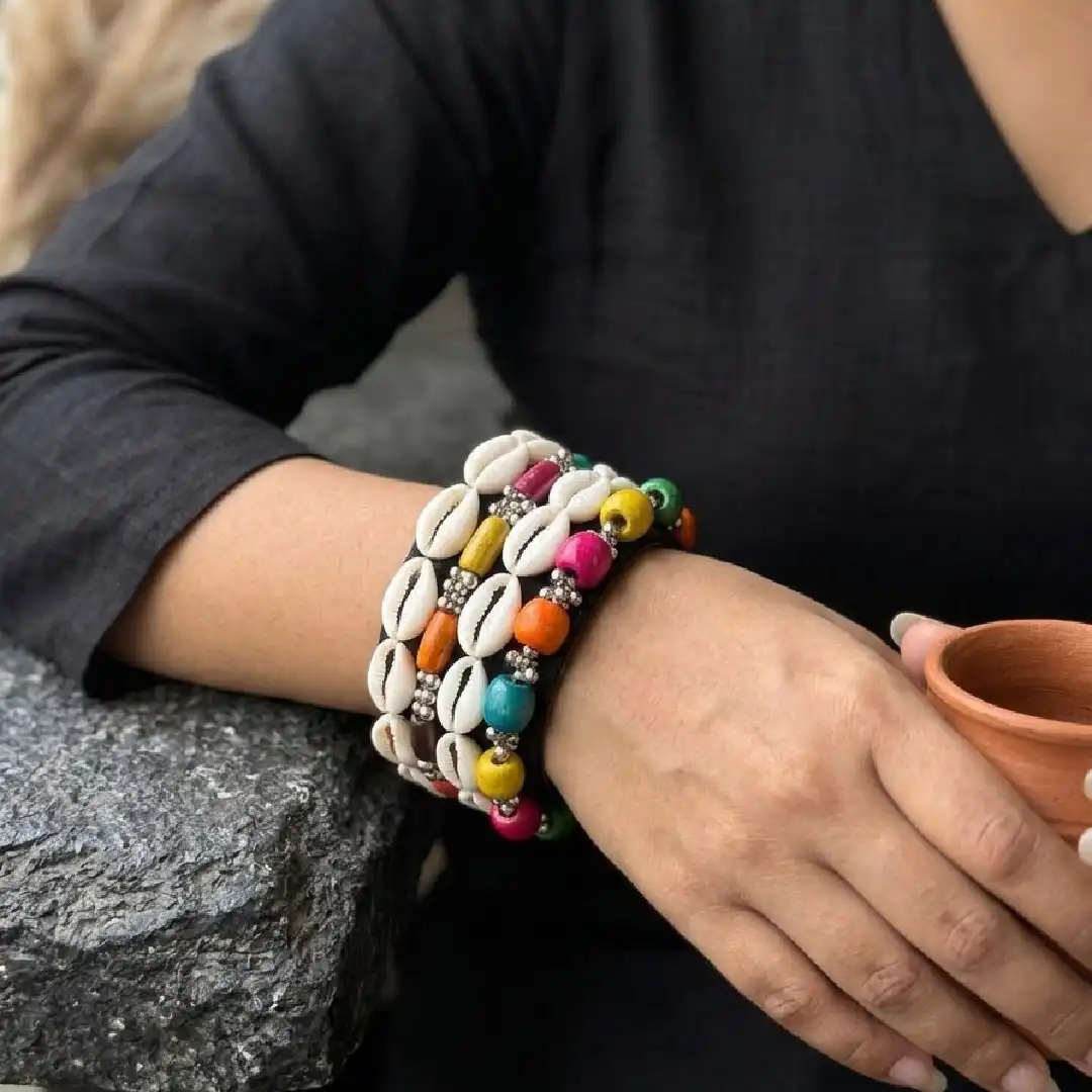 Lifestyle shot of a woman wearing a wide black fabric bangle embellished with rows of white cowrie shells and colorful beads.
