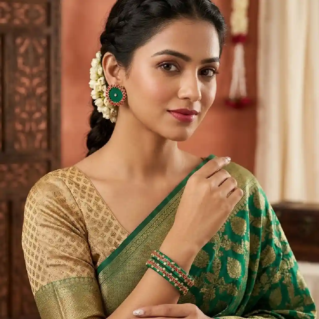 A female model in a green and gold silk saree wearing handcrafted emerald green silk thread bangles and matching large circular Kundan stud earrings with orange-red accents.