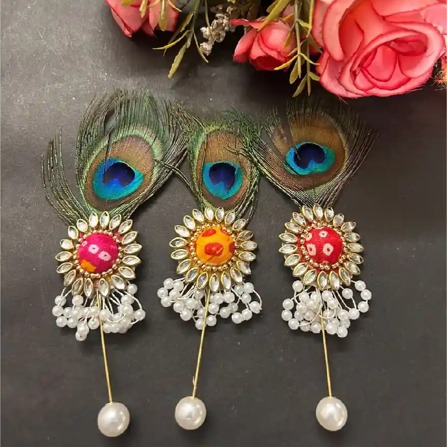 Three handcrafted peacock feather brooches with Kundan centers and pearl drops in pink, yellow, and red colors by ItsyBitsy Kolkata