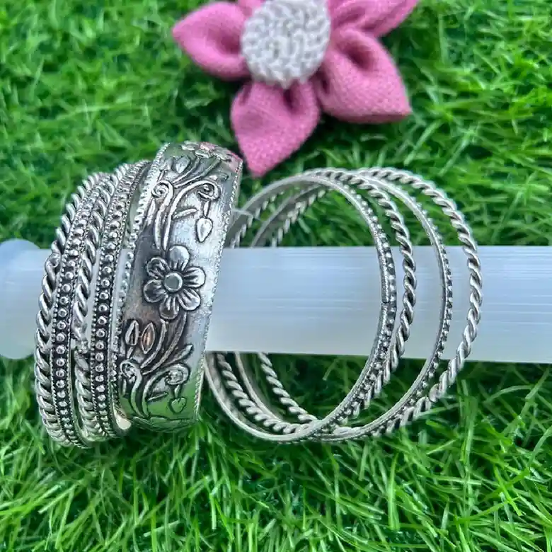 Handcrafted oxidised silver-toned bangle set by Itsy Bitzy Kolkata featuring a broad floral embossed kada and textured thin bangles.