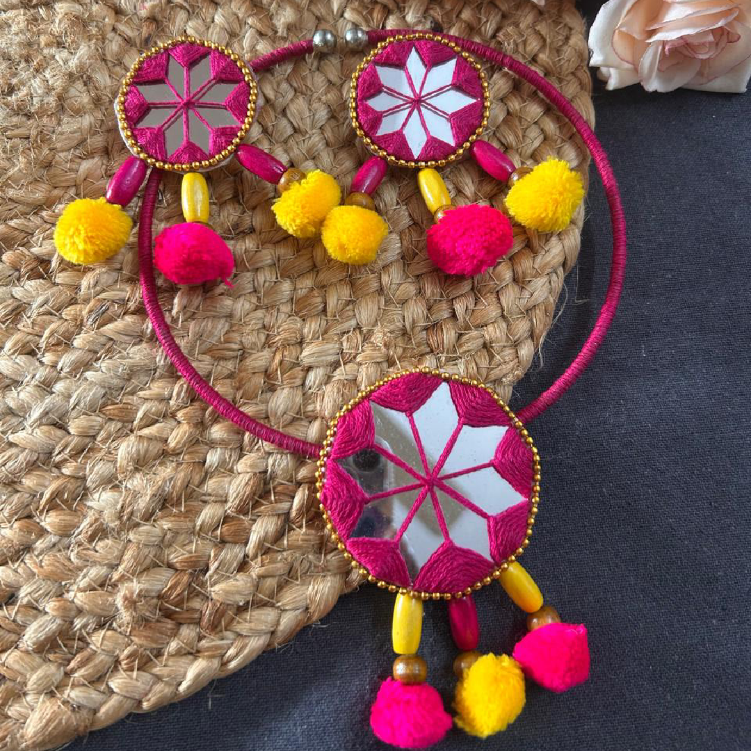 A model showcasing a handcrafted pink thread Hasli choker with star-shaped Lippan mirror work and bright pom-poms from Itsy Bitsy Kolkata, styled with a traditional cream saree during a festive Durga Puja morning.
