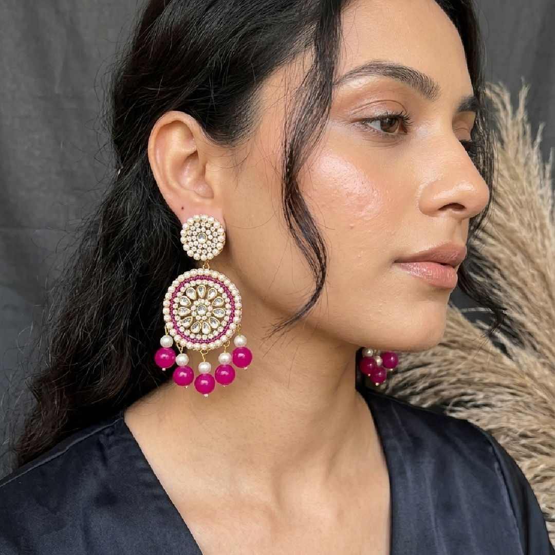 Close-up of a model wearing large round traditional Kundan Chandbali earrings adorned with rani pink beads and hanging white pearls.
